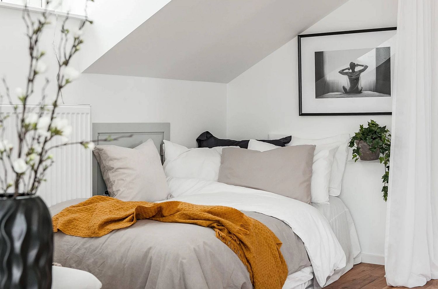 Hình ảnh phòng ngủ với giường nệm màu trắng đặt sát vào góc phòng, rèm cửa màu trắng phân tách với khu vực bên ngoài, chăn mỏng màu vàng tạo điểm nhấn