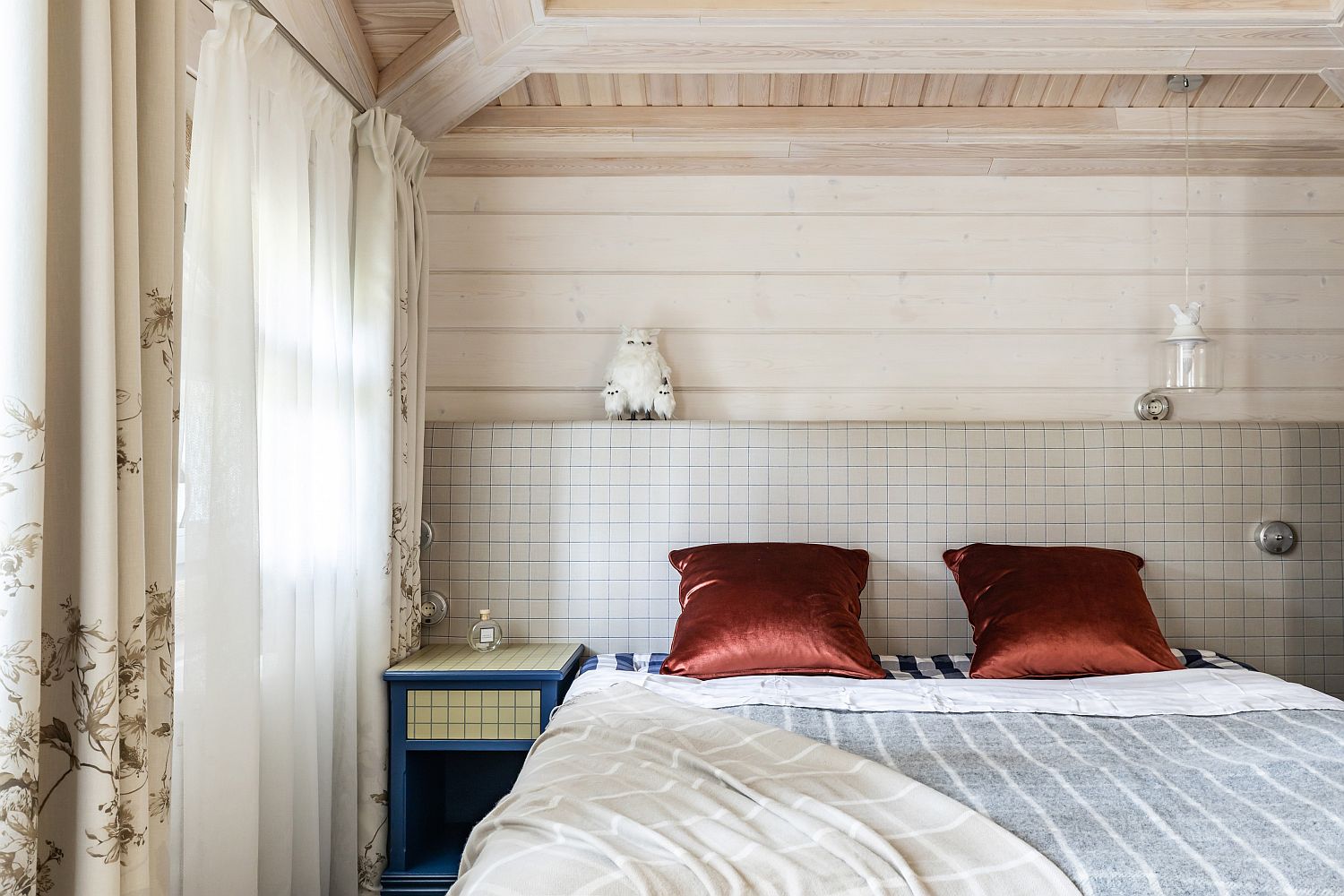 Hình ảnh phòng ngủ nhỏ với giường đặt sát tường ốp gạch, bộ gối màu đồng thau, cạnh đó là rèm cửa hai lớp.
