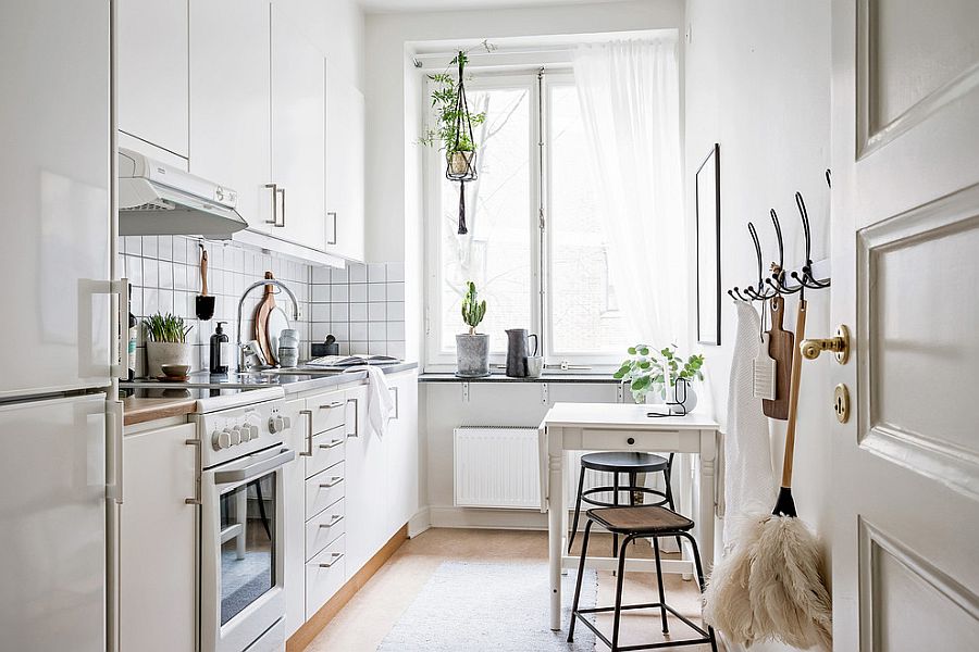 Hình ảnh góc ăn sáng trong phòng bếp màu trắng, trên bàn đặt bình cây xanh, cạnh đó là khung cửa sổ kính