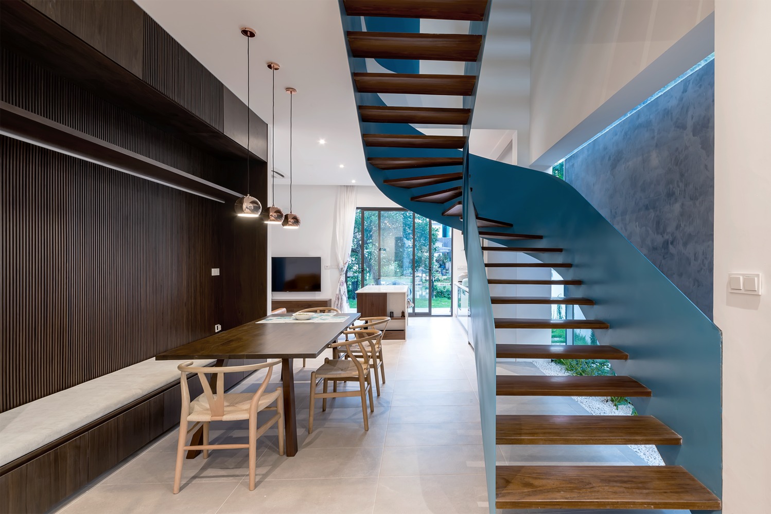 Hình ảnh toàn cảnh phòng ăn cạnh cầu thang với bàn ghế gỗ, băng ghế dài bọc nệm gắn tường ốp gỗ sẫm màu