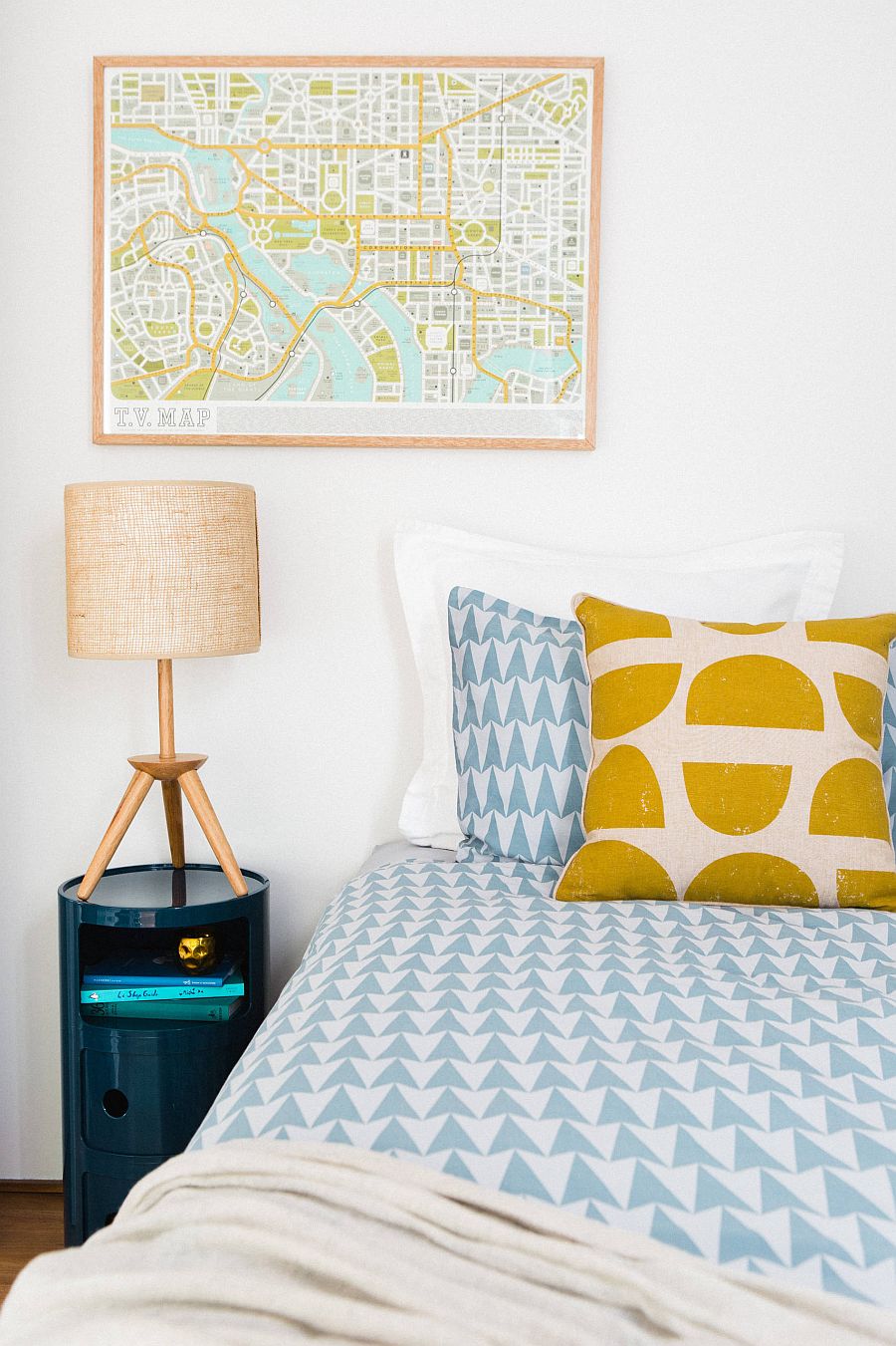 Hình ảnh một góc phòng ngủ với giường nệm êm ái, gối họa tiết chấm bi màu vàng, đèn ngủ màu hồng phấn, bản đồ điểm nhấn