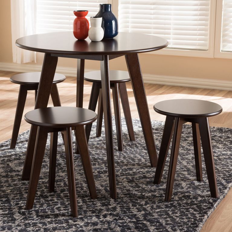 Cận cảnh mẫu bàn ăn bằng gỗ hình tròn đặt trên thảm họa tiết đen trắng, trên bàn đặt 3 bình mùa xanh dương, đỏ, trắng