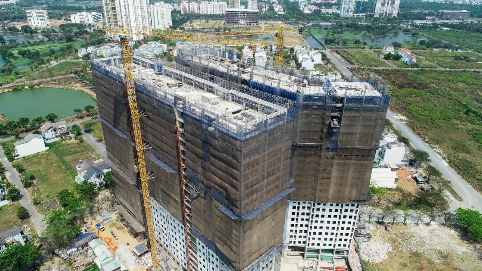 Hình ảnh cận cảnh chụp từ trên cao tòa chung cư cao tầng đang xây dựng, bọc lưới bảo vệ màu xám bên ngoài.