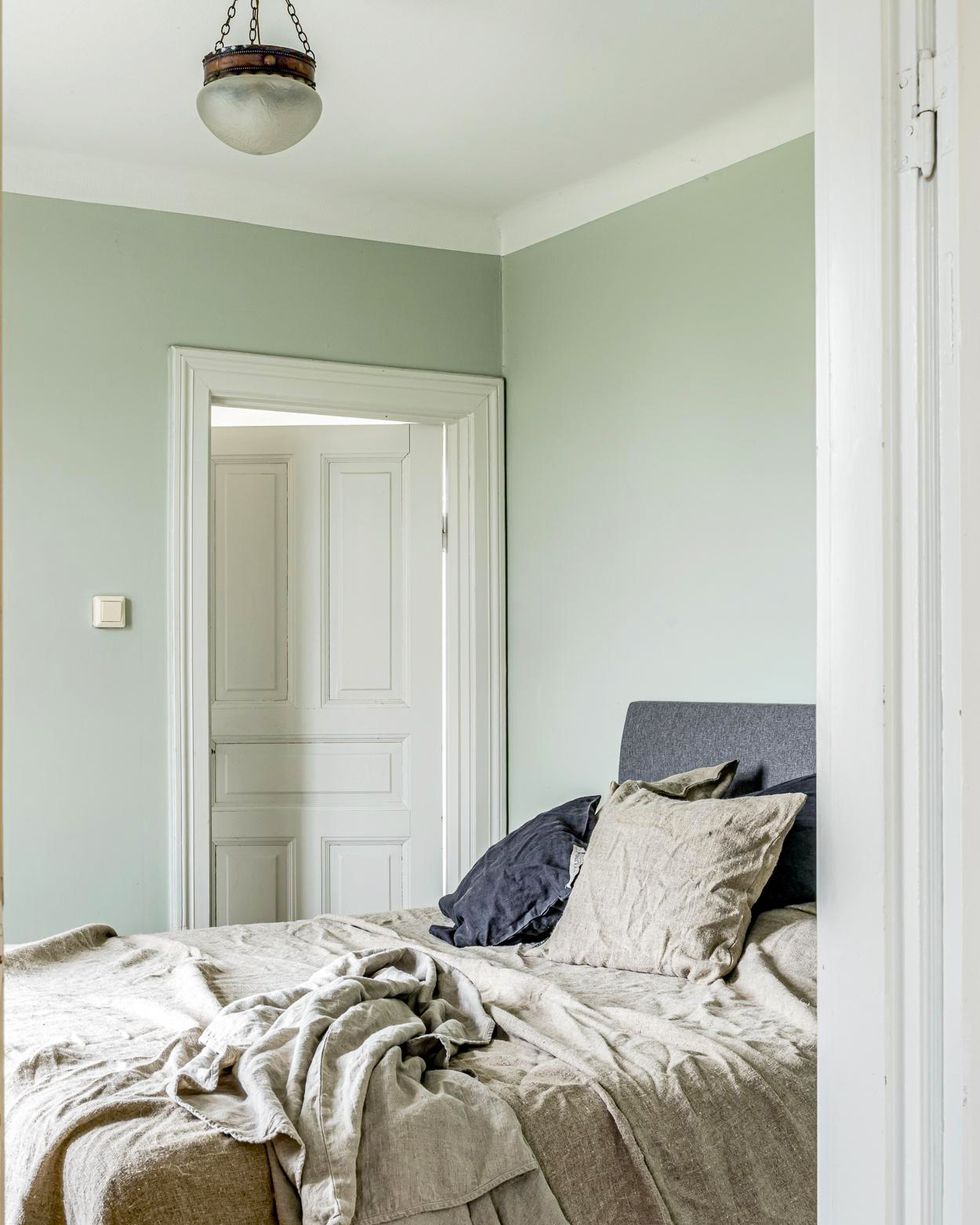 Hình ảnh một góc phòng ngủ với sơn tường màu xanh nhạt, giường nệm màu trắng, đèn thả độc đáo