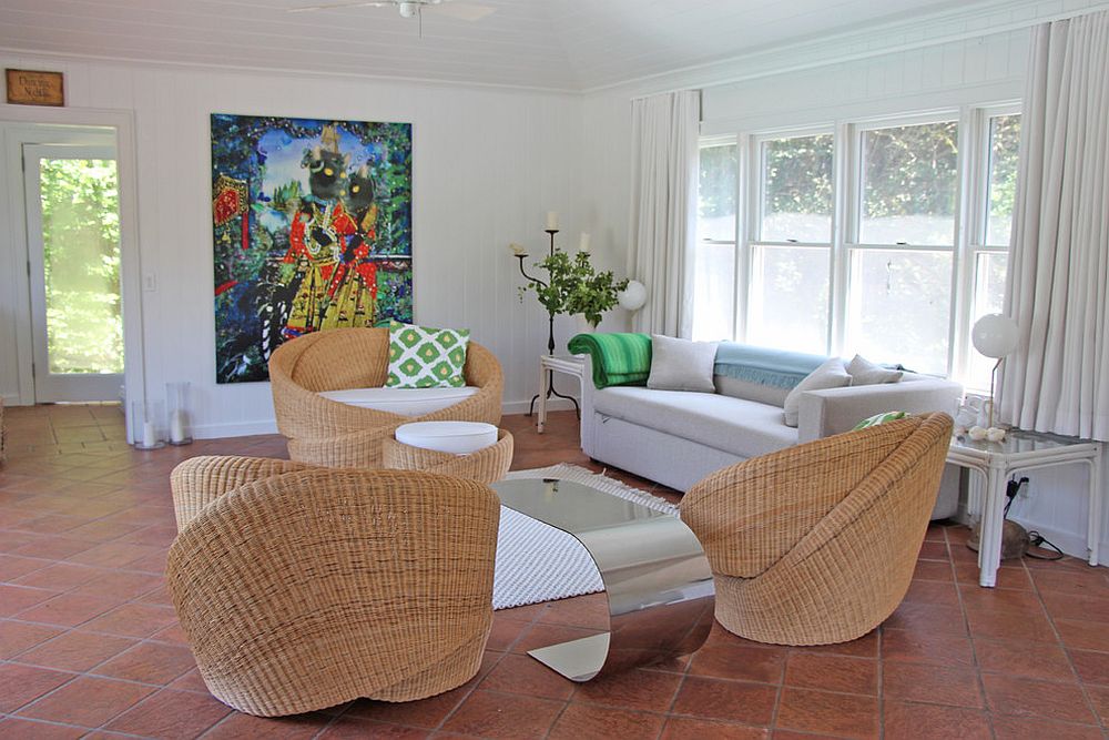 Hình ảnh phòng khách với sàn lát gạch đất nung, sofa cạnh cửa sổ kính, bàn ghế mây tre đan, tranh nghệ thuật treo tường