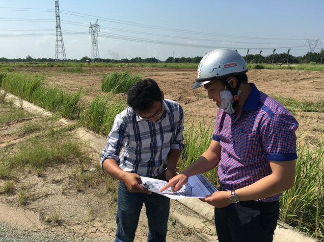 Hình ảnh hai người đàn ông đang đứng xem 1 tấm bản đồ, xung quanh là khu đất rộng bỏ hoang