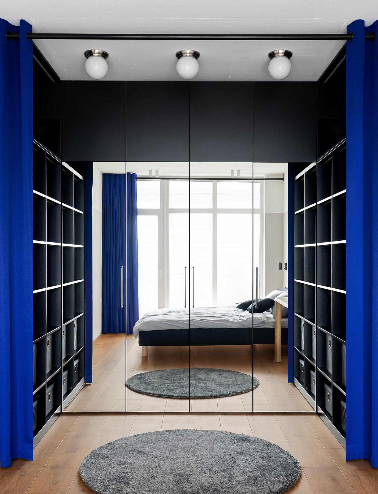Hình ảnh cận cảnh phòng thay đồ tích hợp trong phòng ngủ với kệ mở cao kịch trần, phân tách bởi rèm cửa màu xanh coban