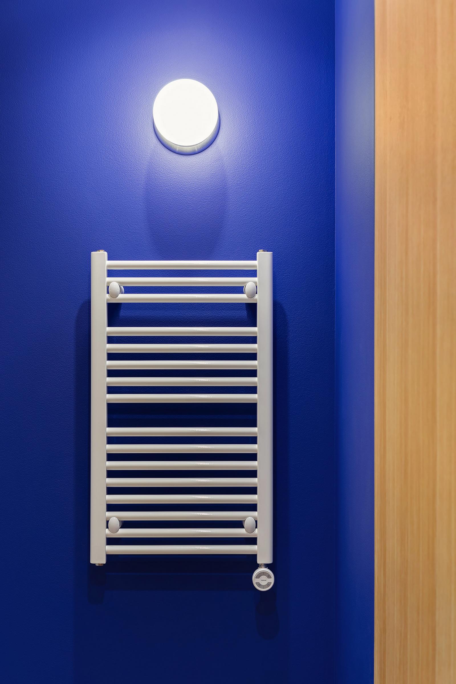 Hình ảnh cận cảnh mảng tường trong căn hộ 65m2 sơn màu xanh coban, đèn tường ánh sáng trắng