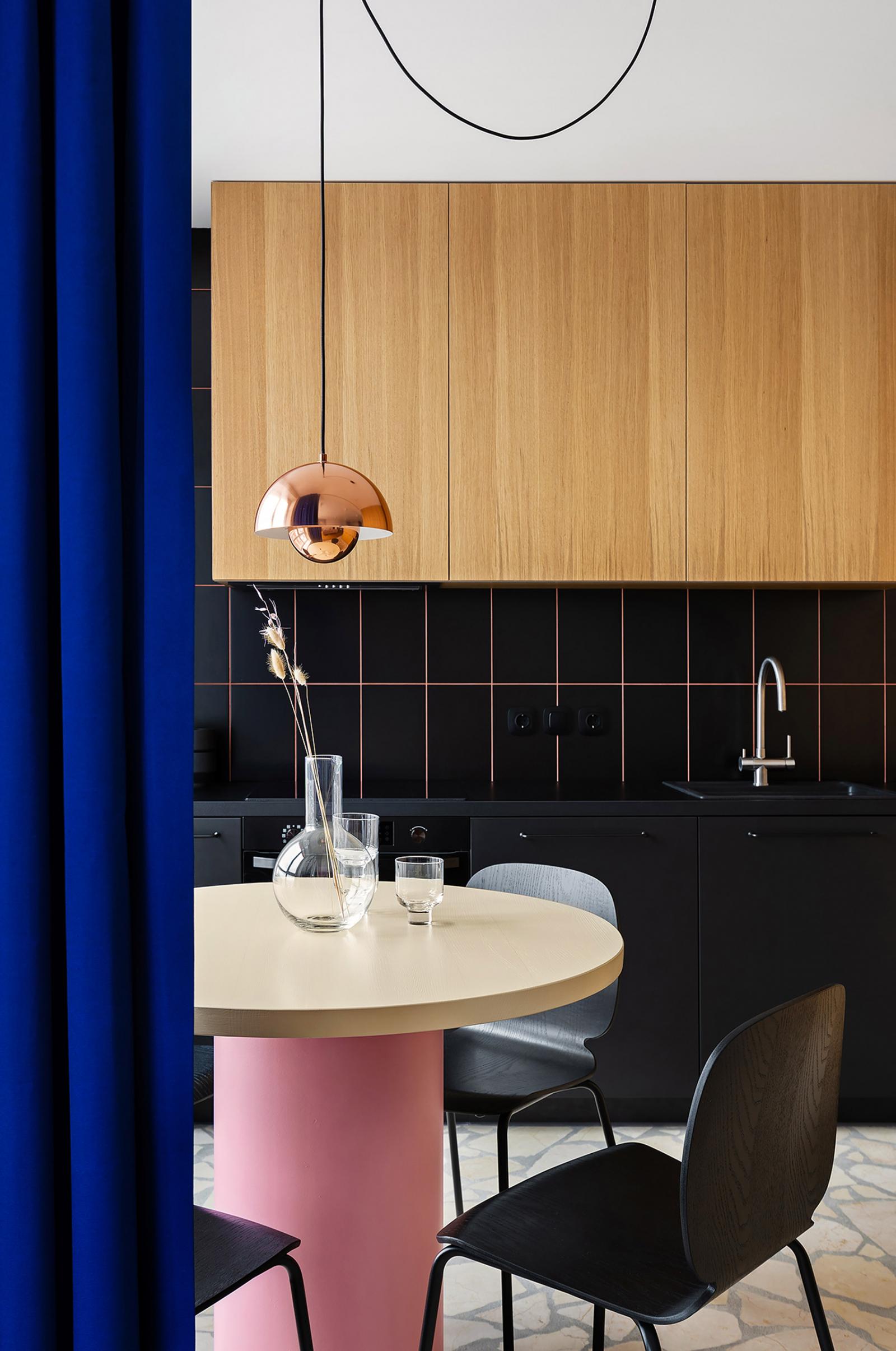 Hình ảnh một góc phòng bếp căn hộ 65m2 với bàn tròn màu hồng, tủ gỗ, rèm cửa màu xanh coban