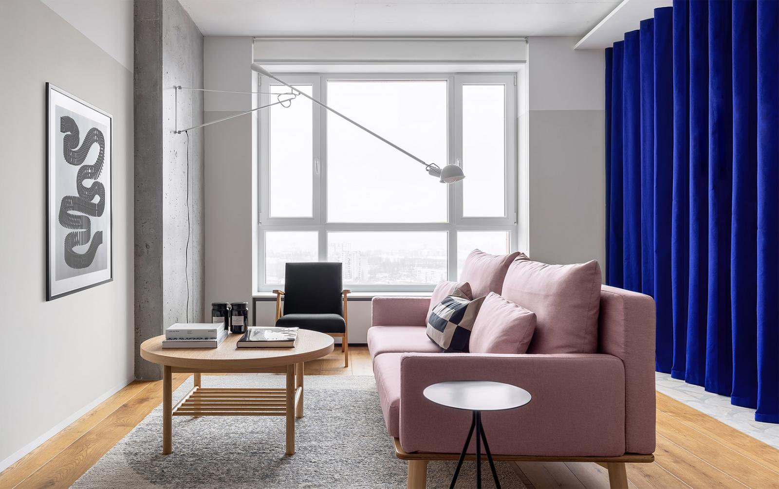 Hình ảnh toàn cảnh phòng khách căn hộ với sofa màu hồng, bàn trà gỗ, ghế tựa màu đen, tranh nghệ thuật treo tường