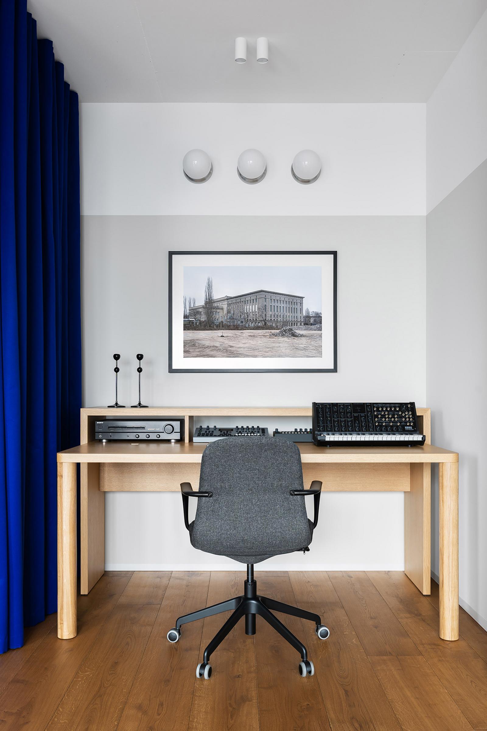 Hình ảnh toàn cảnh phòng làm việc tại nhà được bài trí đơn giản, ngăn nắp với bàn gỗ màu sáng, ghế xoay và bức tranh tường tạo điểm nhấn