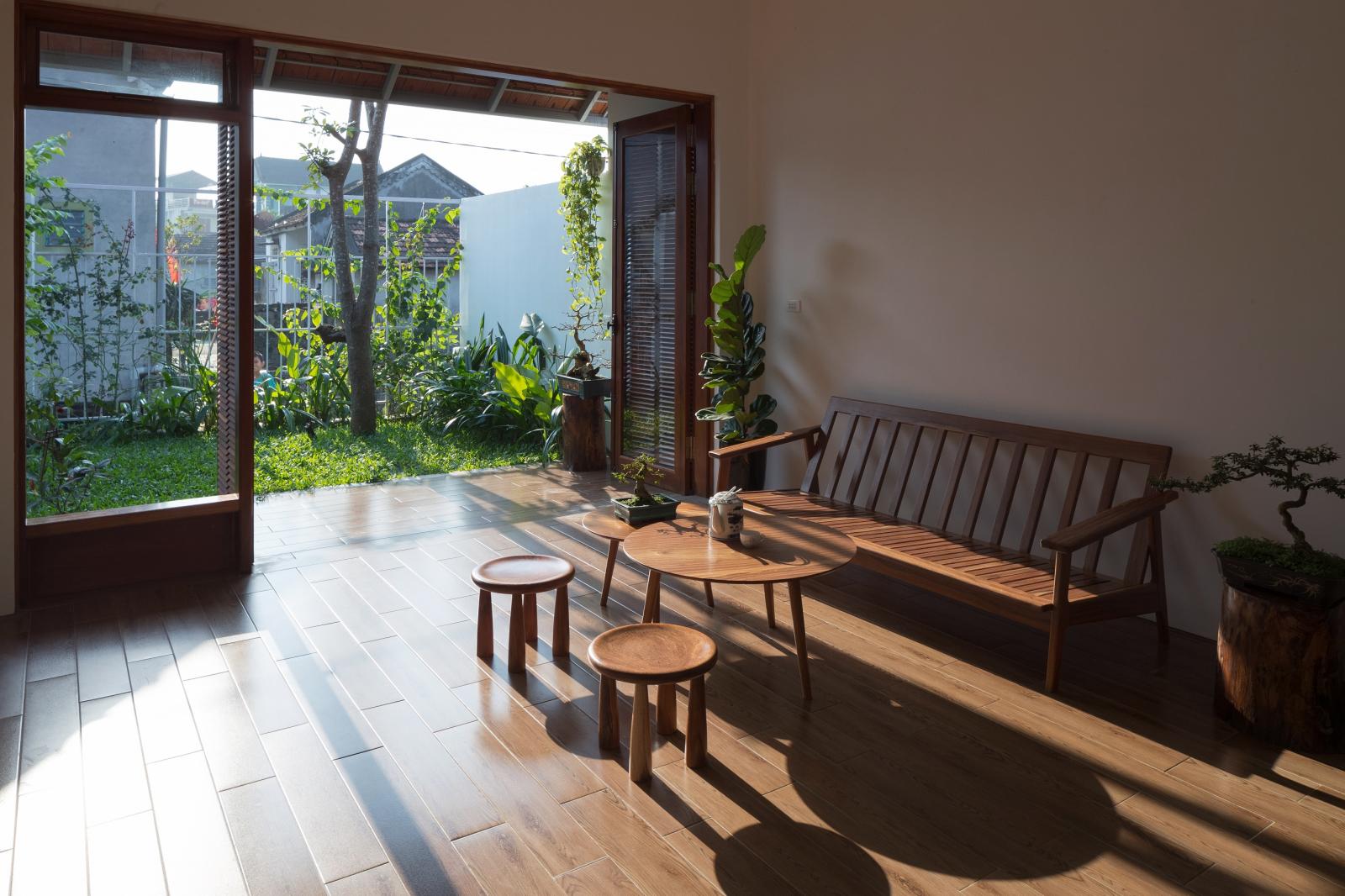 Hình ảnh phòng khách ngập tràn ánh nắng với sofa gỗ, bàn trà tròn, cửa lớn mở ra sân vườn