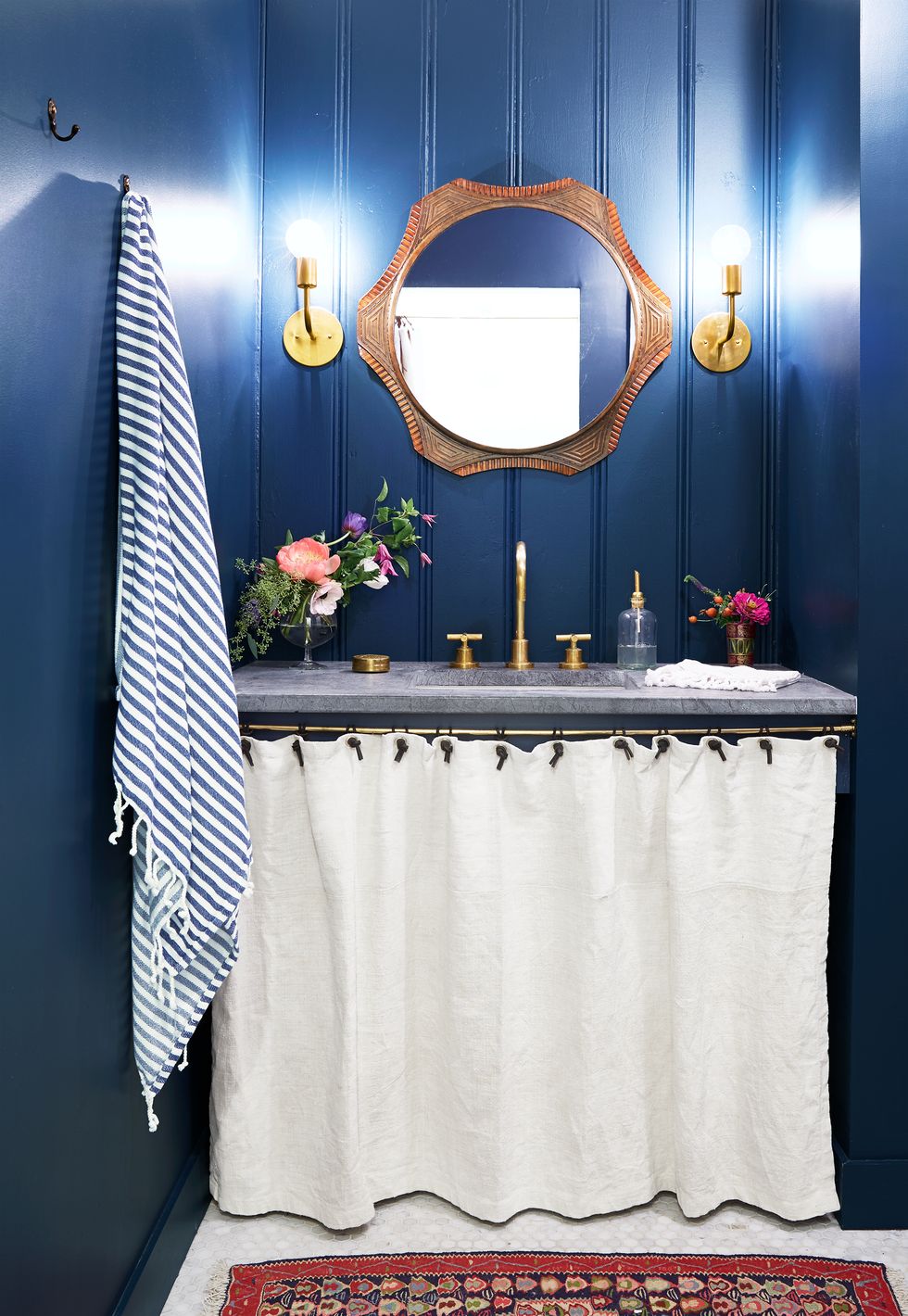 Hình ảnh phòng tắm với tường sơn màu xanh đậm, rèm vải màu trắng, thảm trải thổ cẩm, khung gương gỗ