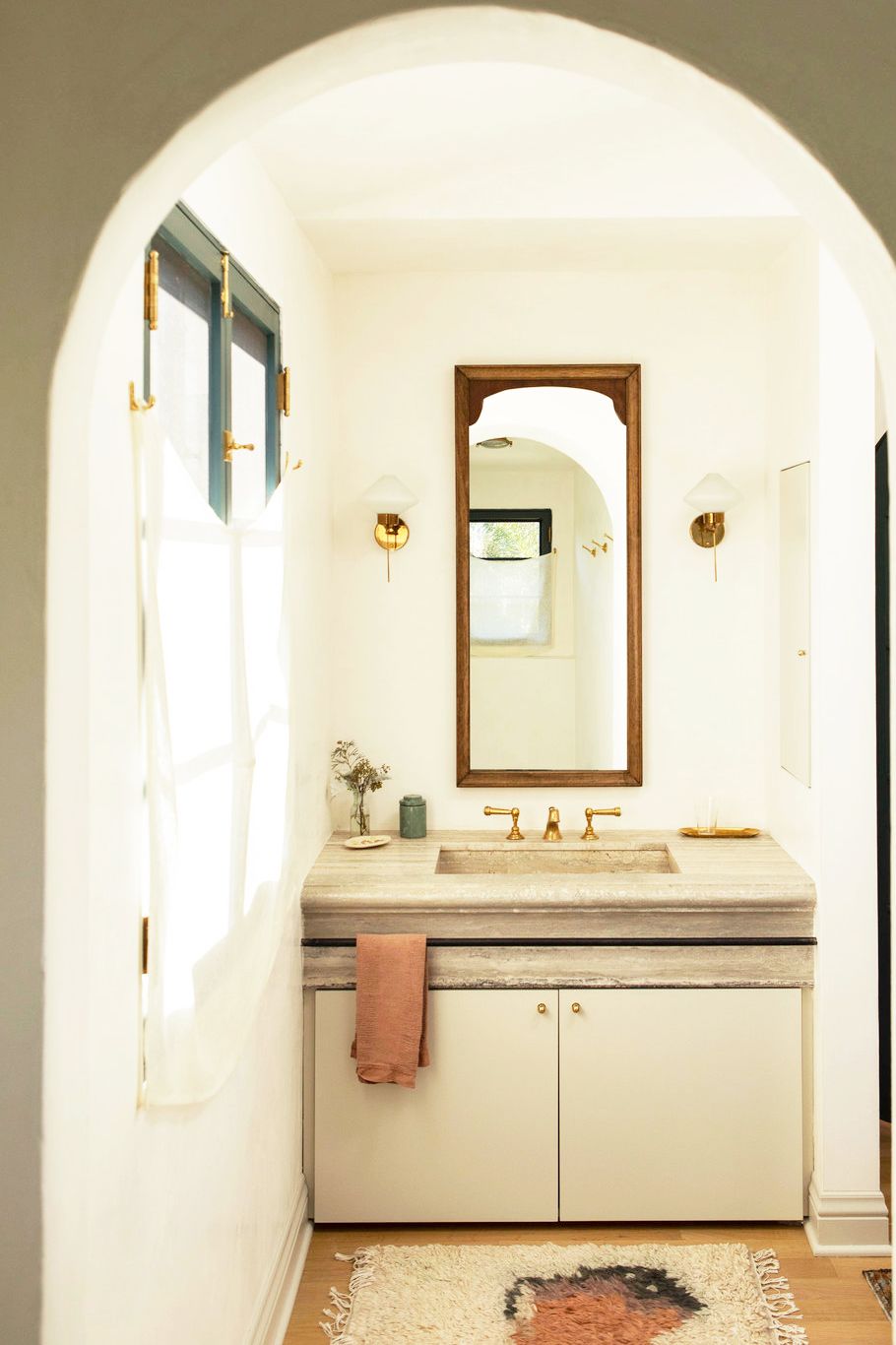 Hình ảnh bên trong phòng tắm nhỏ màu kem với cửa sổ sơn xanh, rèm trắng