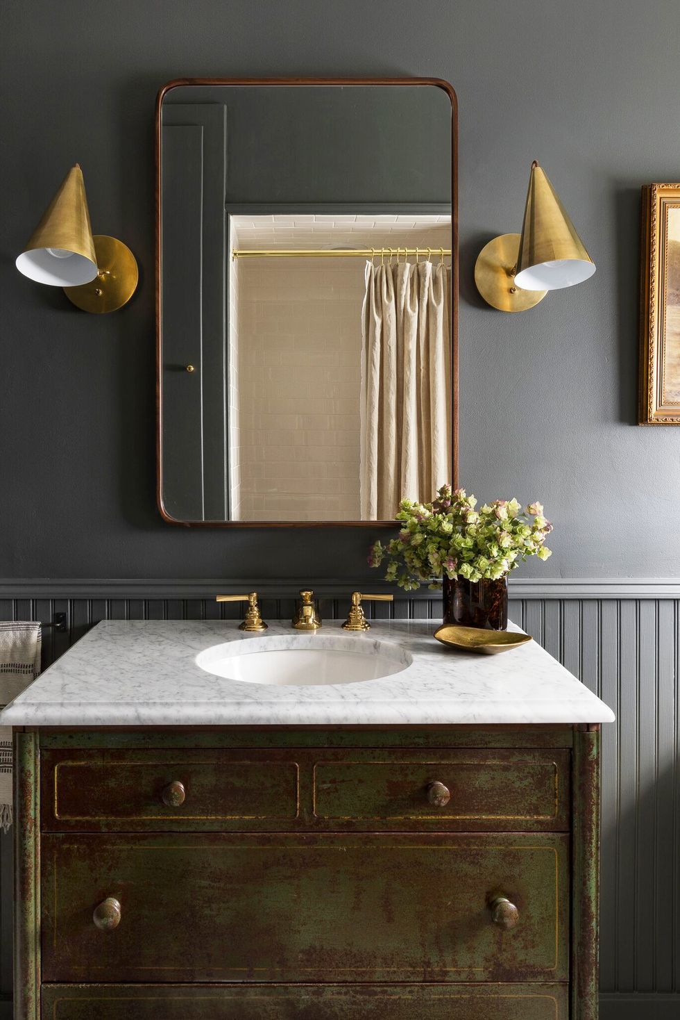 Hình ảnh phòng tắm nhỏ tông màu xám đậm bắt mắt, bề mặt bồn rửa bằng đá cẩm thạch, khung gương lớn, bộ đôi đèn tường kim loại vàng