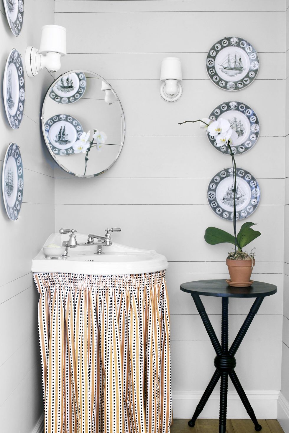 Hình ảnh phòng tắm nhỏ màu xám sáng với đĩa gốm sứ trang trí tường, dưới bồn rừa lắp thêm rèm vải giấu dọn vật dụng bên trong