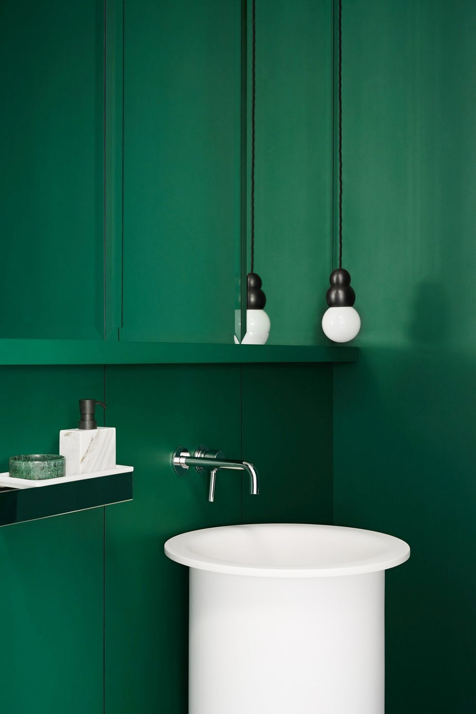 Hình ảnh phòng tắm với sắc xanh lá cây bao phủ tường, bồn rửa và đèn thả màu trắng nổi bật