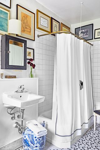 Hình ảnh một góc phòng tắm với rèm cửa màu trắng bao xung quanh bồn tắm, tường trang trí rất nhiều khung tranh