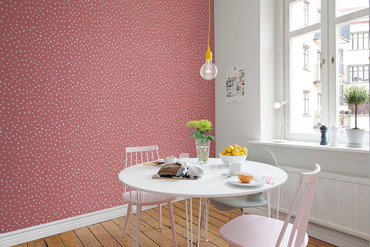 Hình cảnh cận cảnh bộ bàn ăn hình tròn đặt cạnh bức tường màu hồng chấm trắng, đèn thả sợi đốt tạo điểm nhấn