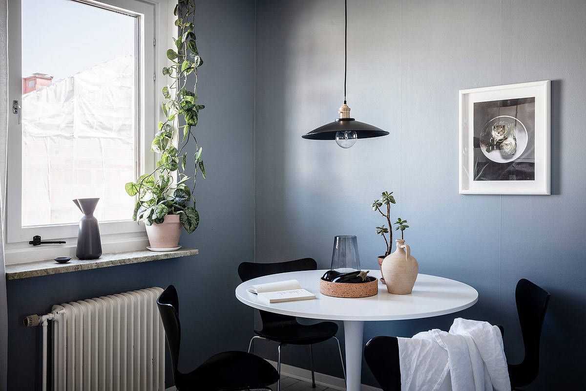 Hình ảnh phòng ăn với tường sơn màu xanh nhạt, bàn tròn nhỏ màu trắng kết hợp ghế đen đặt cạnh cửa sổ kính