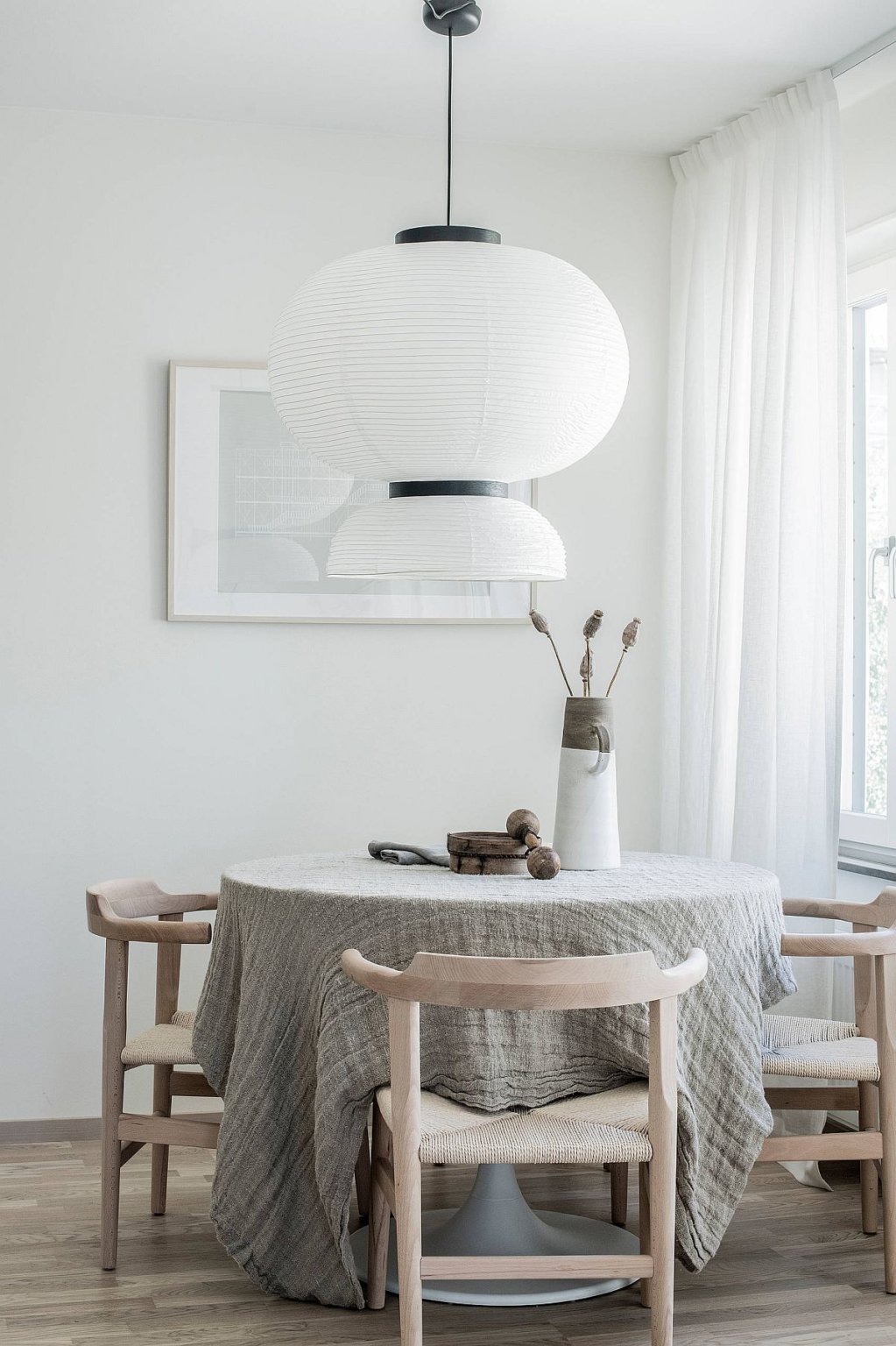 Hình ảnh phòng ăn nhỏ màu trắng với bàn gỗ tròn phủ khăn trải xám, đèn thả khổ lớn tạo điểm nhấn ấn tượng