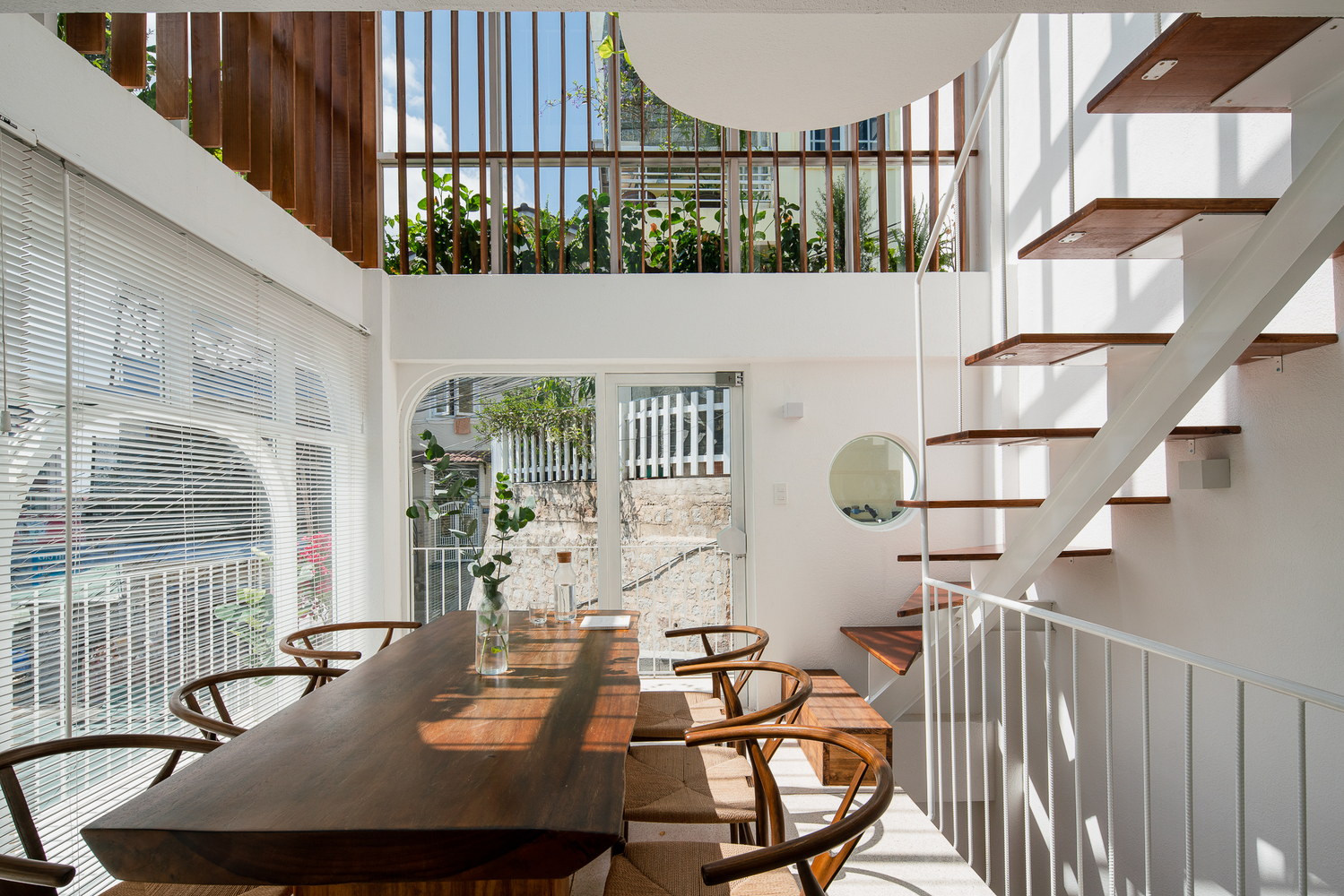 Hình ảnh không gian phòng ăn ngập tràn ánh sáng với bàn ghế gỗ, lam gỗ, cửa sổ kính trong suốt, cạnh đó là cầu thang dẫn lên tầng trên
