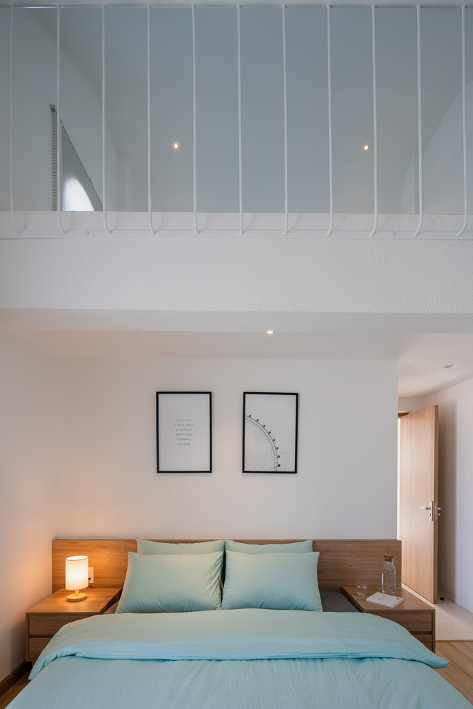 Hình ảnh một góc phòng ngủ trong homestay với ga gối màu xanh lam, tranh trang trí đầu giường, hai táp gỗ hai bên