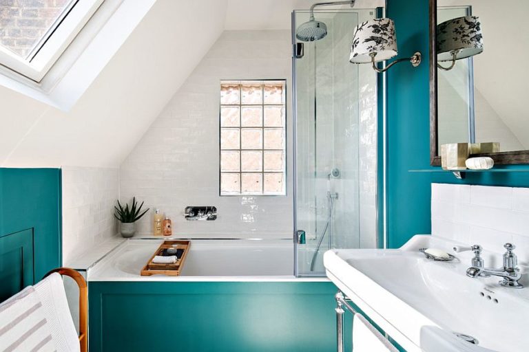Hình ảnh phòng tắm tầng áp mái thoáng sáng với cửa sổ mái, bồn tắm nằm, tủ kệ lưu trữ, sắc xanh lam đậm tạo điểm nhấn