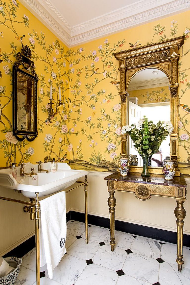 Hình ảnh phòng tắm phong cách đồng quê với tường trang trí bằng giấy dán màu vàng họa tiết hoa lá, chim muông, bồn rửa, khung gương, tủ kệ có khung kim loại sáng bóng