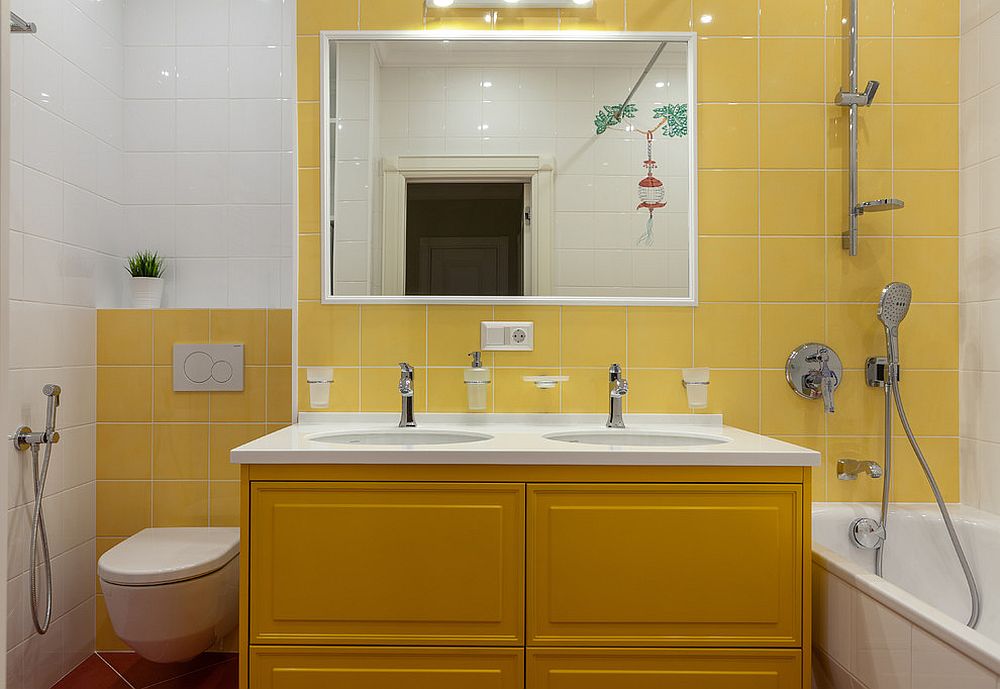 Hình ảnh một góc phòng tắm với tường ốp gạch vàng, gương lớn, tủ vanity màu vàng đậm hơn