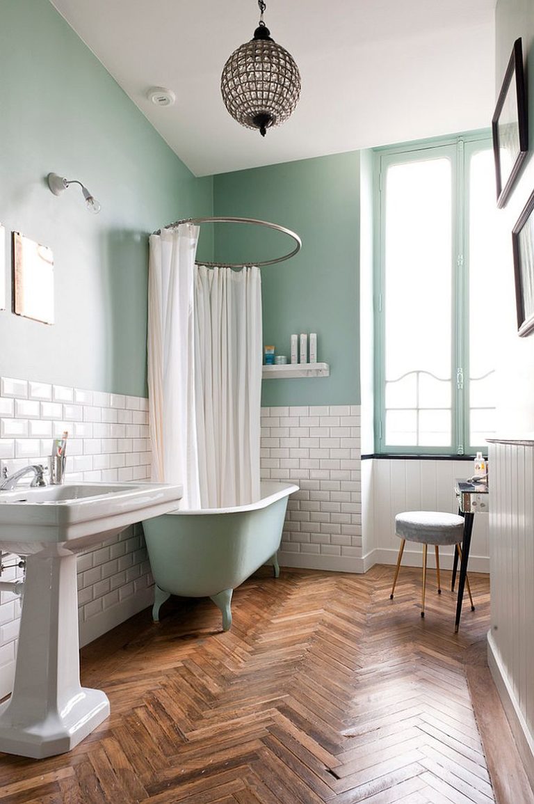 Hình ảnh phòng tắm với nửa tường phía trên sơn xanh pastel, nửa tường còn lại màu trắng, sàn gỗ xương cá bắt mắt