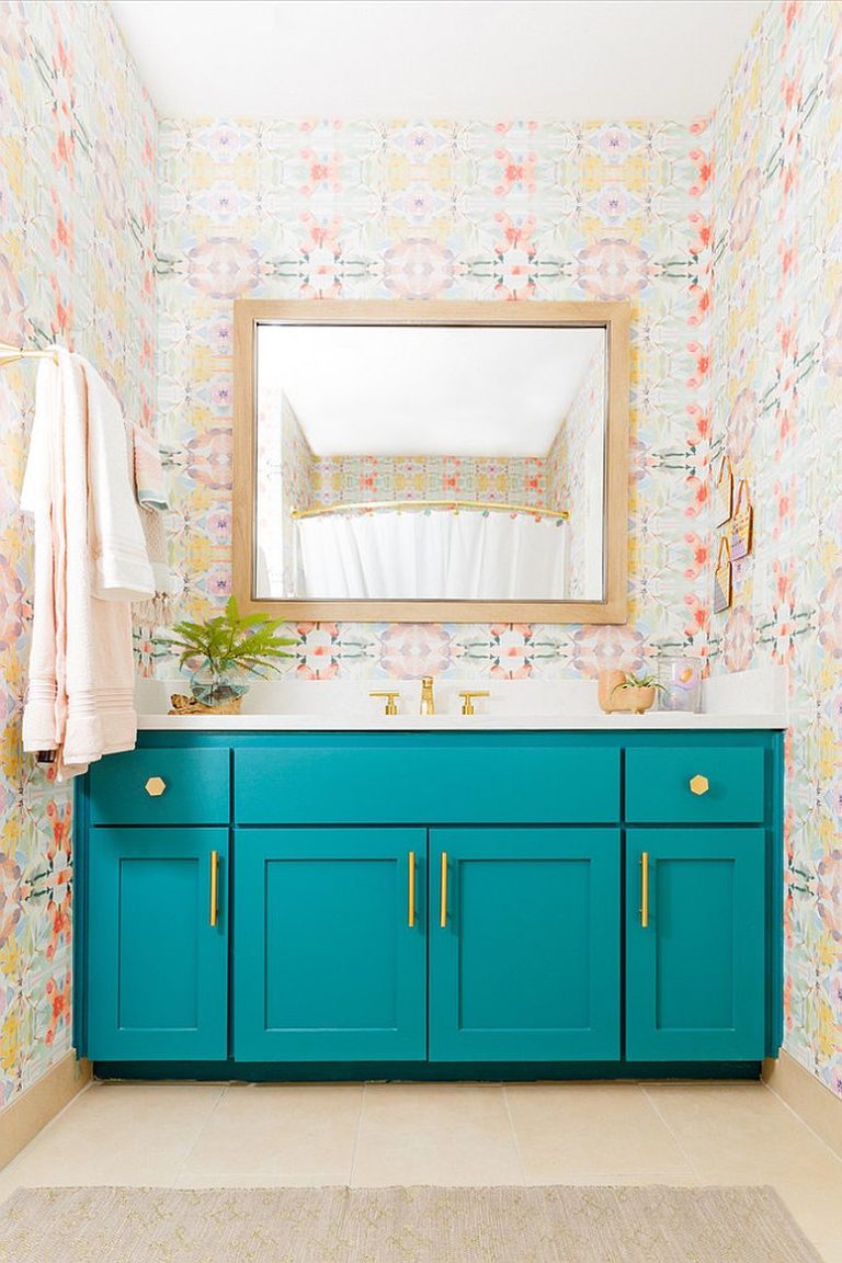 Hình ảnh phòng tắm nhỏ với tủ đựng màu xanh lam, tường dán giấy họa tiết hoa, gương soi gắn tường