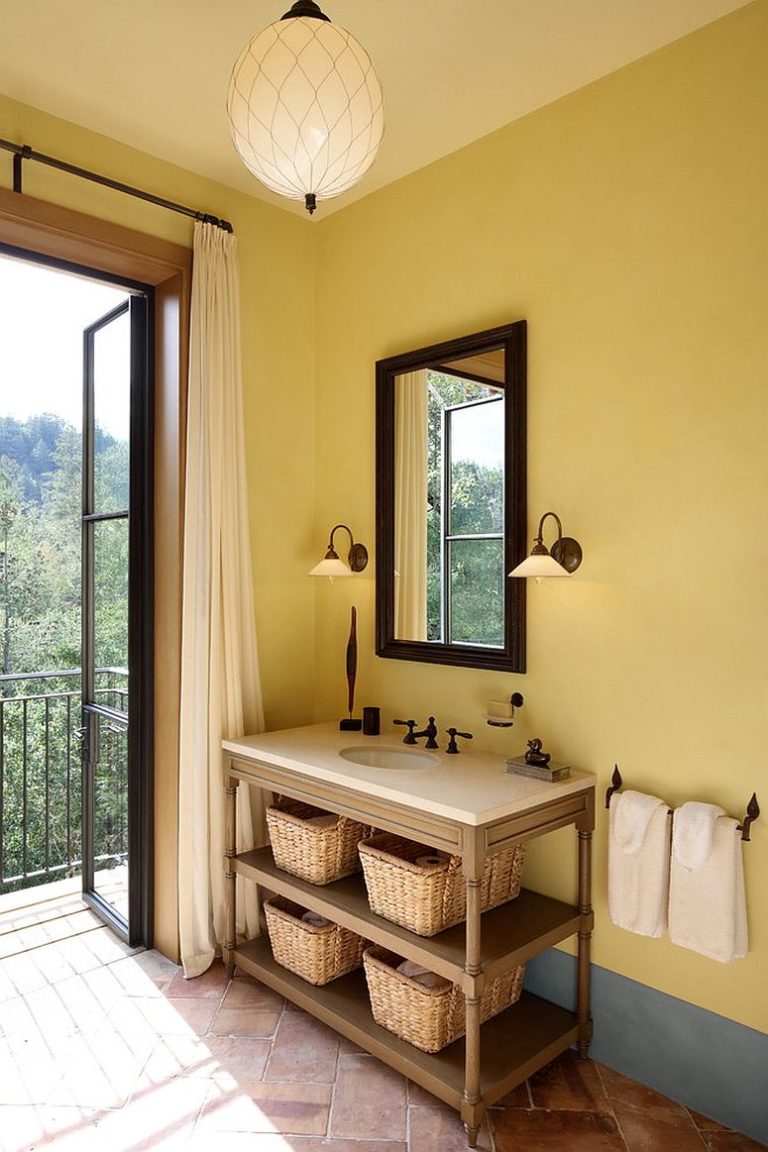 Hình ảnh một góc phòng tắm phong cách Địa Trung Hải với tường sơn màu vàng nhạt, đèn trần họa tiết quả trám, giỏ mây đựng đồ