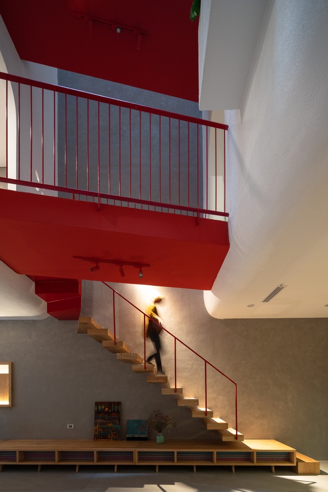 Hình ảnh một người đang bước đi trên cầu thang gỗ bậc rỗng xuống tầng hầm, lan can sắt sơn đỏ, trần sơn đỏ