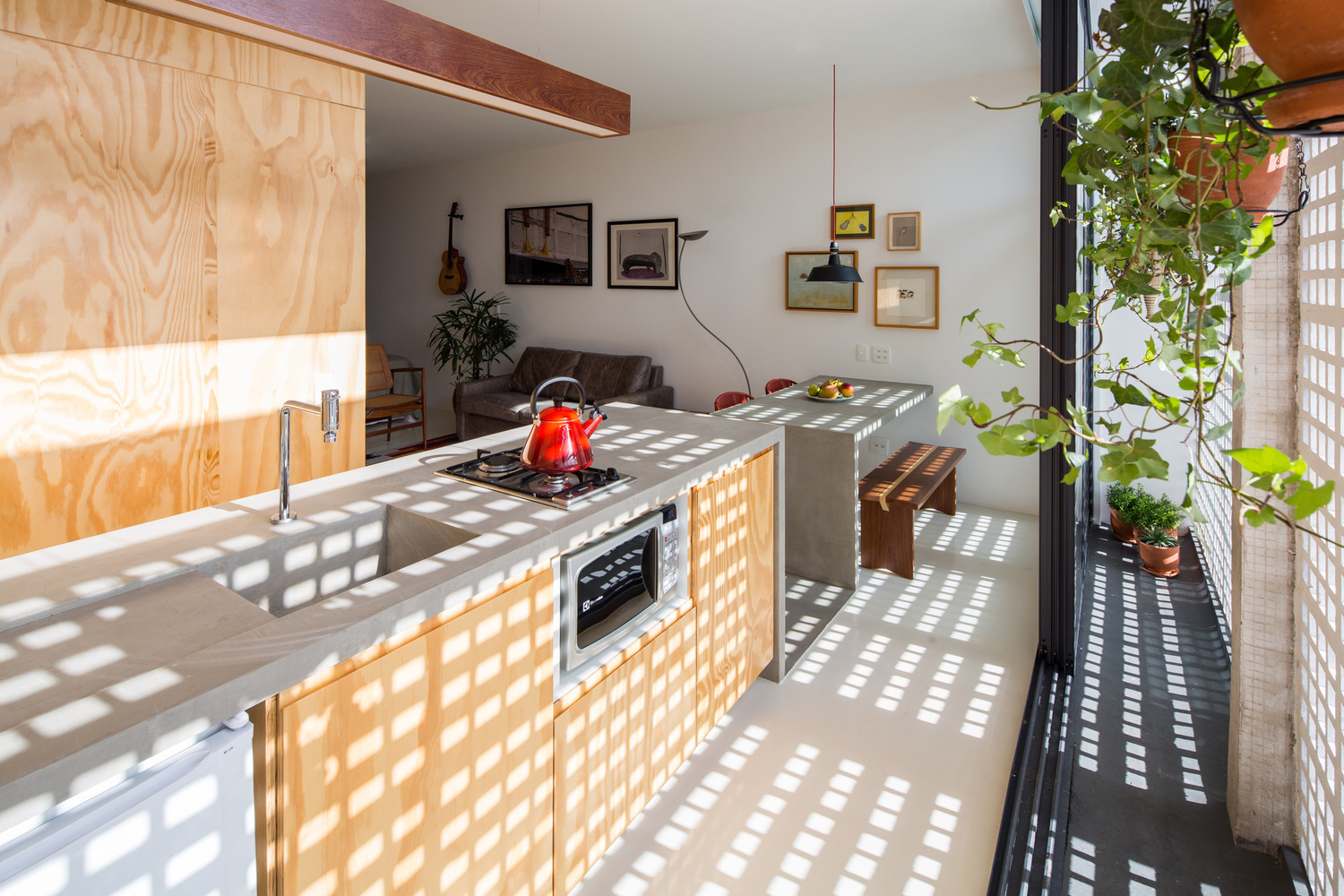 Hình ảnh một phòng bếp ngập tràn ánh sáng với tường chắn, mặt tủ bếp bằng gỗ, trên bếp đặt ấm đun nước màu đỏ