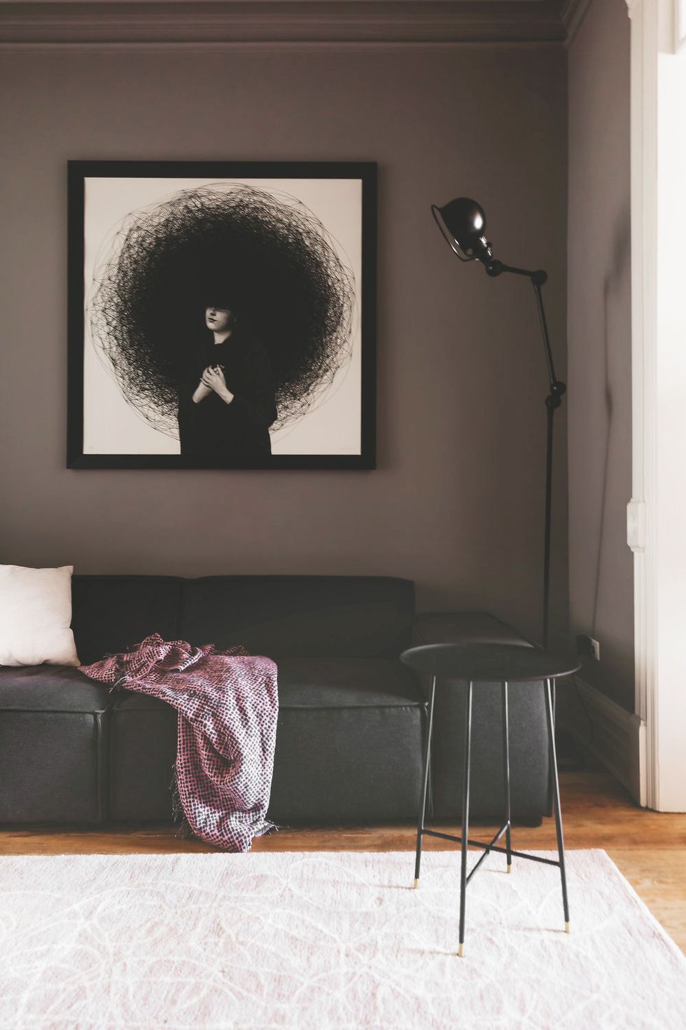 Hình ảnh một góc phòng khách với tường màu tím, sofa và bàn trà màu đen ấn tượng, tranh treo tường độc đáo