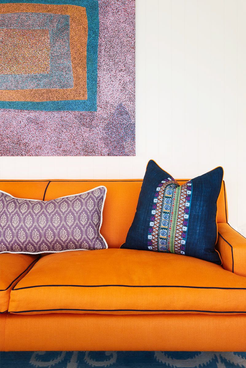 Một góc phòng khách với sofa màu cam, gối tựa tím oải hương cùng tông với tranh tường
