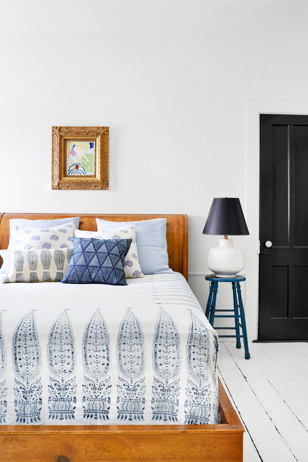 Hình ảnh một góc phòng ngủ với ga gối màu trắng họa tiết xanh dương, cạnh đó là bàn đặt đèn ngủ 