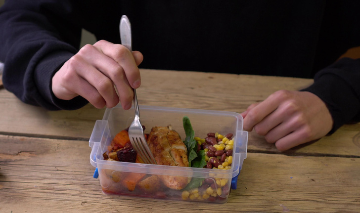 Hình ảnh cận cảnh một người mặc áo màu đen đang dùng thìa xúc thức ăn đựng trong hộp nhựa