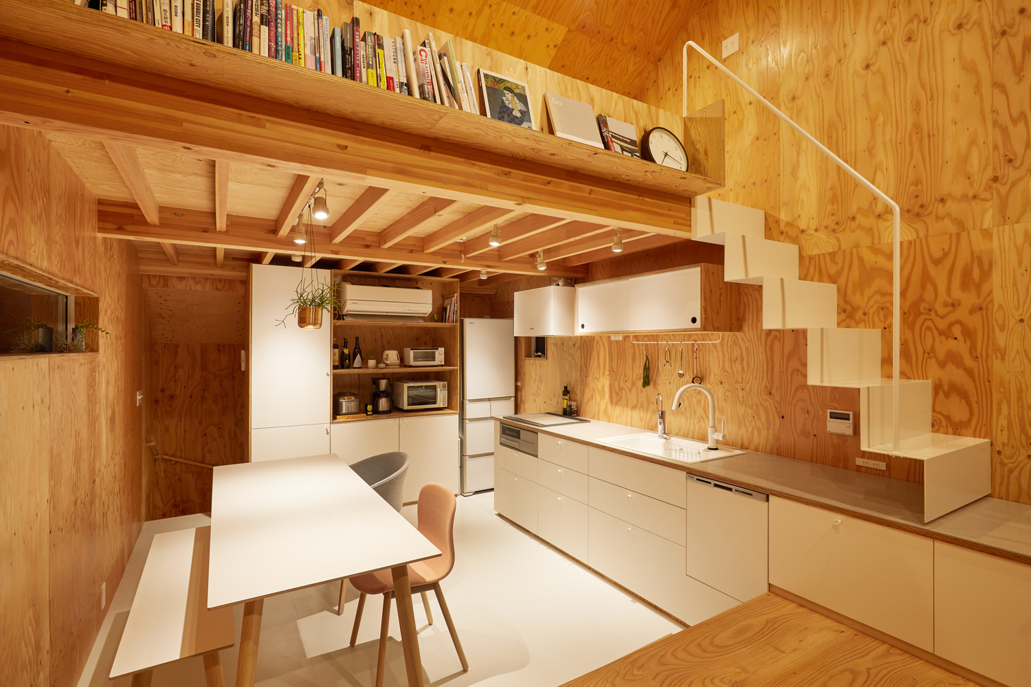 Hình ảnh phòng bếp với tủ kệ lưu trữ và bàn ăn sơn trắng, cạnh đó là cầu thang dẫn lên gác xép