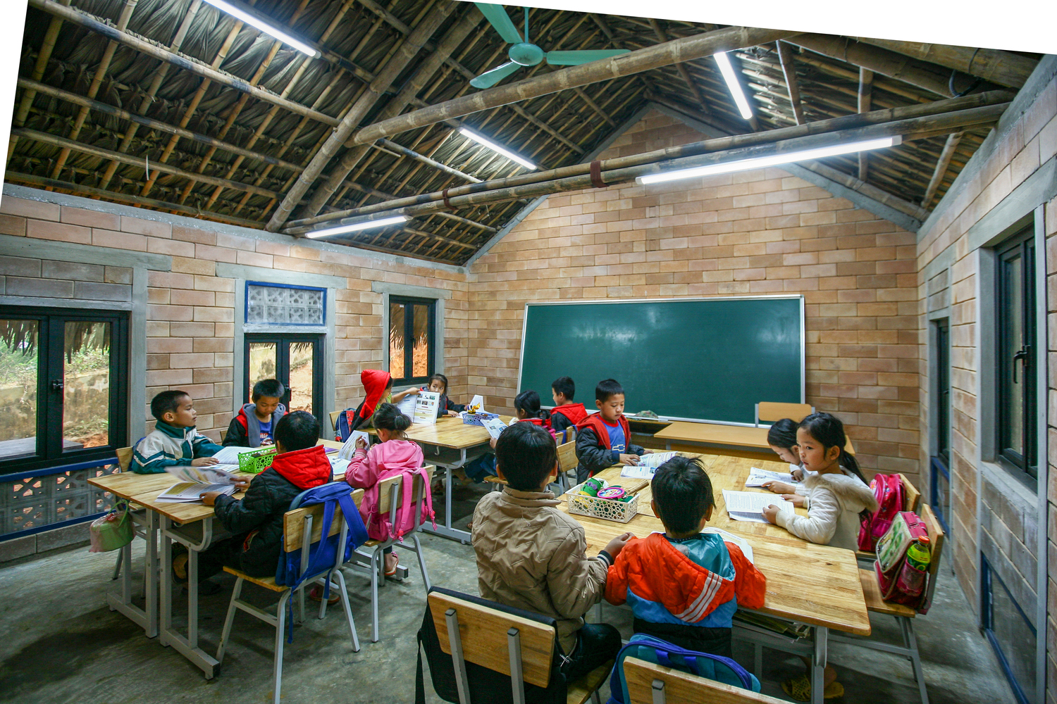 Hình ảnh bên trong lớp học với mái lợp mái, tường gạch, bàn ghế gỗ