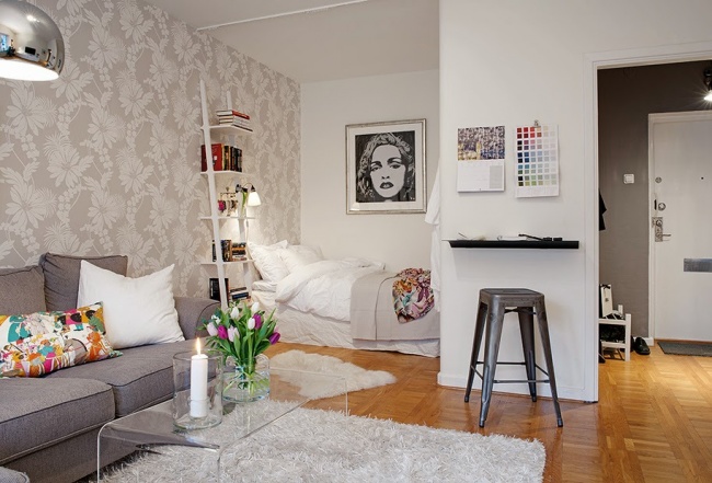 Hình ảnh bên trong căn hộ studio với giấy dán tường họa tiết hoa lá, hốc ngủ treo tranh chân dung đen trắng, thang lưu trữ, cạnh đó là phòng khách