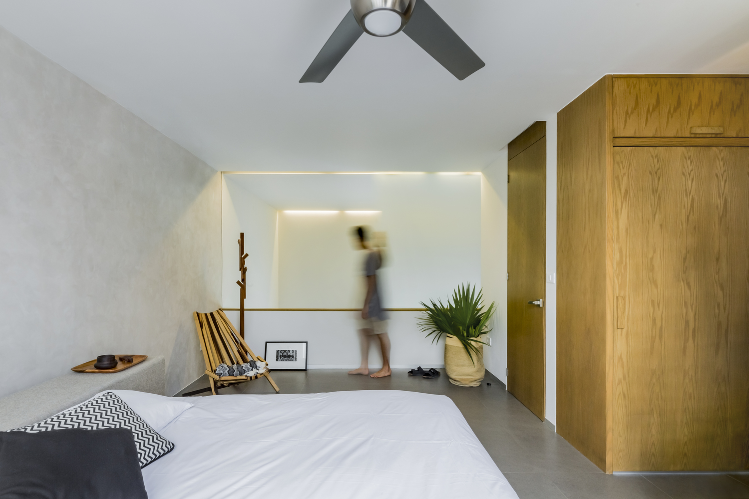 Hình ảnh phòng ngủ có thiết kế đơn giản với ga gối màu trắng, tủ gỗ cao kịch trần, chậu cây lớn đặt ở góc phòng