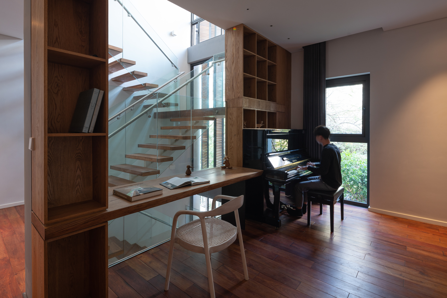 Hình ảnh góc làm việc và thư giãn cạnh cửa sổ kính thoáng sáng với đàn piano, bàn gỗ, tường kính