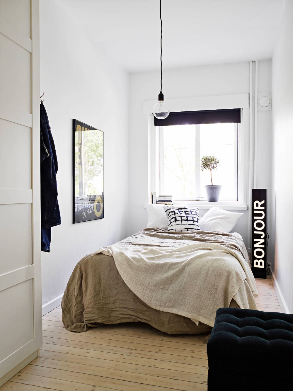 Hình ảnh phòng ngủ nhỏ phong cách tối giản với ga gối màu trắng chủ đạo, tranh treo tường, cửa sổ đầu giường