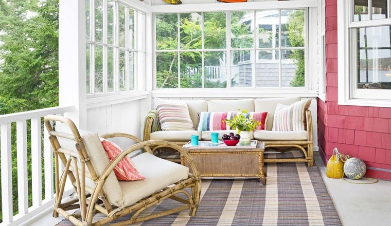 Hình ảnh hiên nhà được bài trí đẹp mắt với bàn ghế mây tre đan, gối tựa màu sắc, thảm trải kẻ sọc, chậu cây xanh