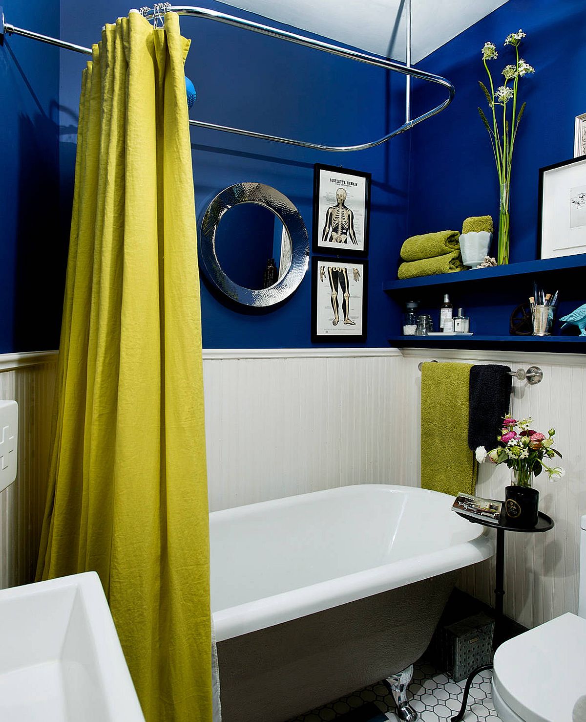 hình ảnh phòng tắm nhỏ với mảng tường sơn xanh đậm, bồn tắm màu trắng, rèm cửa và khăn màu vàng nổi bật