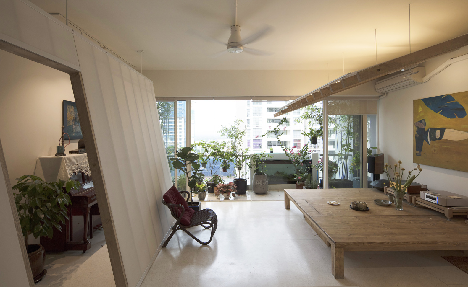 hình ảnh toàn cảnh phòng sinh hoạt chung trong căn hộ với phản gỗ, cây xanh ngập tràn, tường kính, ghế thư giãn