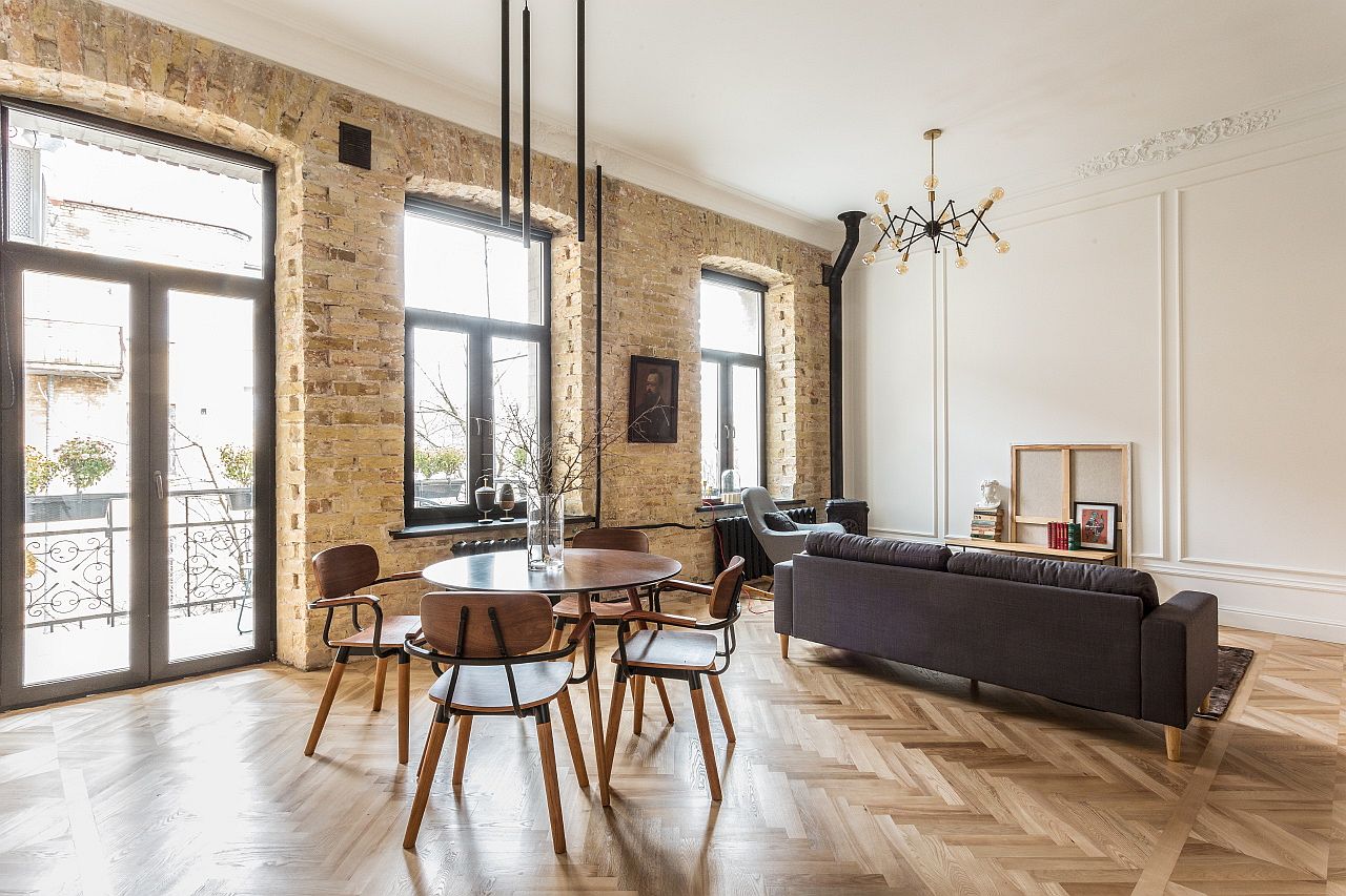 hình ảnh toàn cảnh phòng khách và phòng ăn trong căn hộ hiện đại với bàn ăn tròn, sofa ghi xám, tường gạch thô, cửa sổ kính