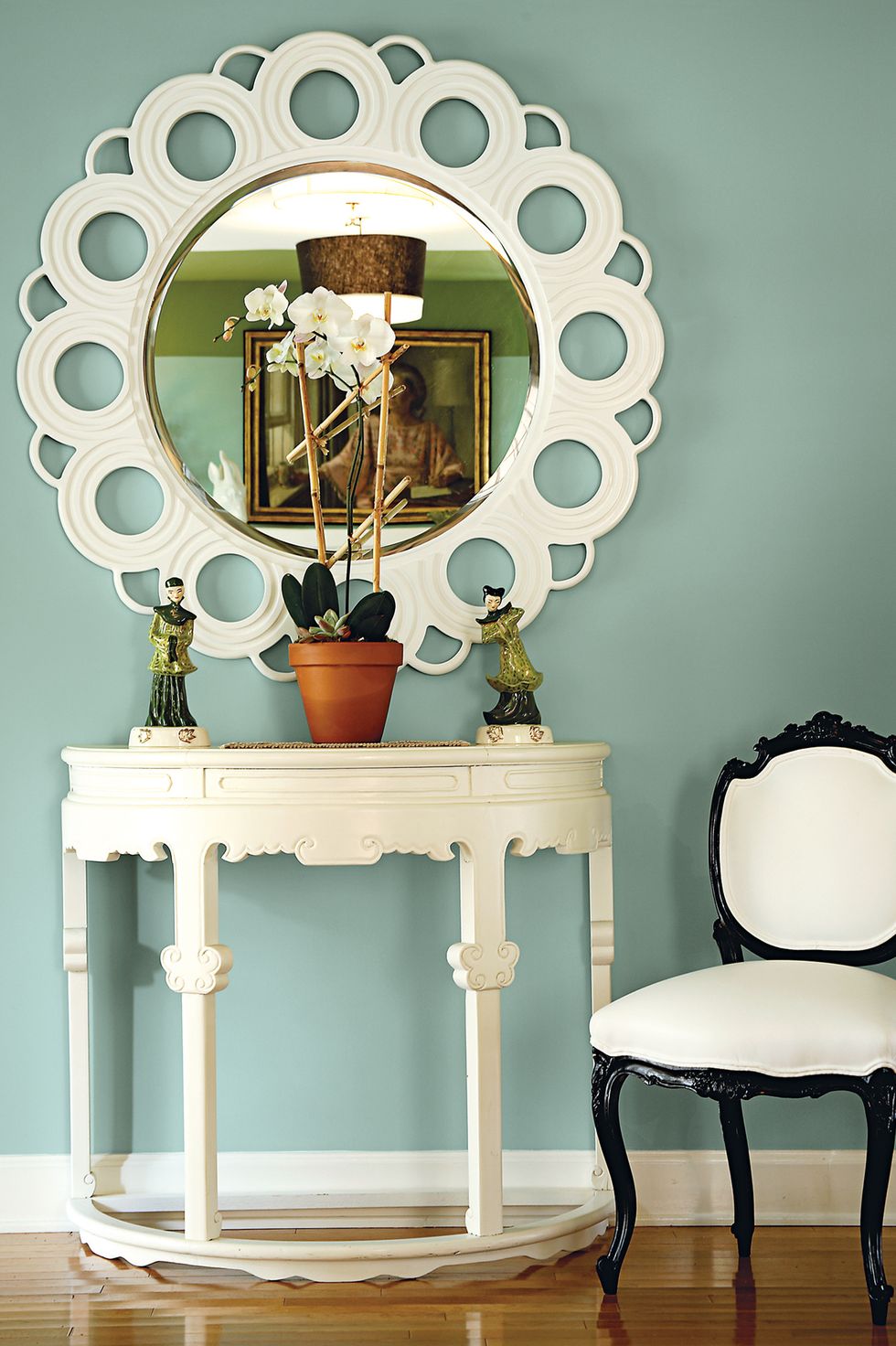 hình ảnh một góc nhà với bàn gương trăng điểm màu trắng, ghế ngồi khung đen, chậu cây trang trí, tượng điêu khắc nhỏ, tường màu xanh lam